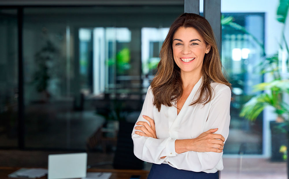 Líder empresarial sonriendo cruzada de brazos frente despacho