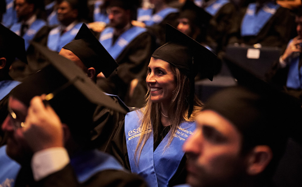 Un grupo de graduadas y graduados en una ceremonia de fin de estudios de master, luciendo togas negras y estolas azules. Esta escena simboliza el acceso igualitario a la educación superior y la preparación académica de mujeres para liderar en el mundo empresarial.