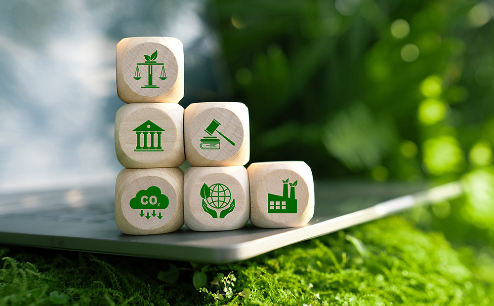 La imagen presenta seis bloques de madera con íconos verdes que representan conceptos clave del derecho ambiental, como la justicia ecológica, las instituciones gubernamentales, la regulación legal, la reducción de emisiones de CO₂, la sostenibilidad global y la industria energética. Esta composición visual refleja los pilares fundamentales del marco jurídico que guía la transición energética, destacando la importancia de las leyes ambientales en la promoción de modelos energéticos más sostenibles y responsables.