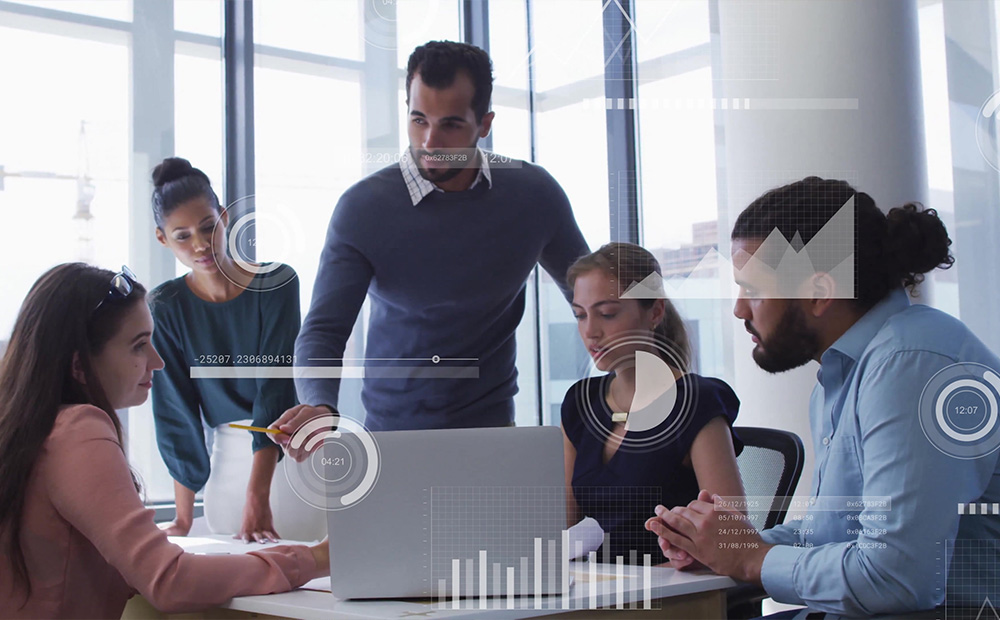 La imagen presenta a un equipo reunido alrededor de un portátil, acompañado de gráficos digitales superpuestos que representan datos, análisis y flujos de información en tiempo real. 