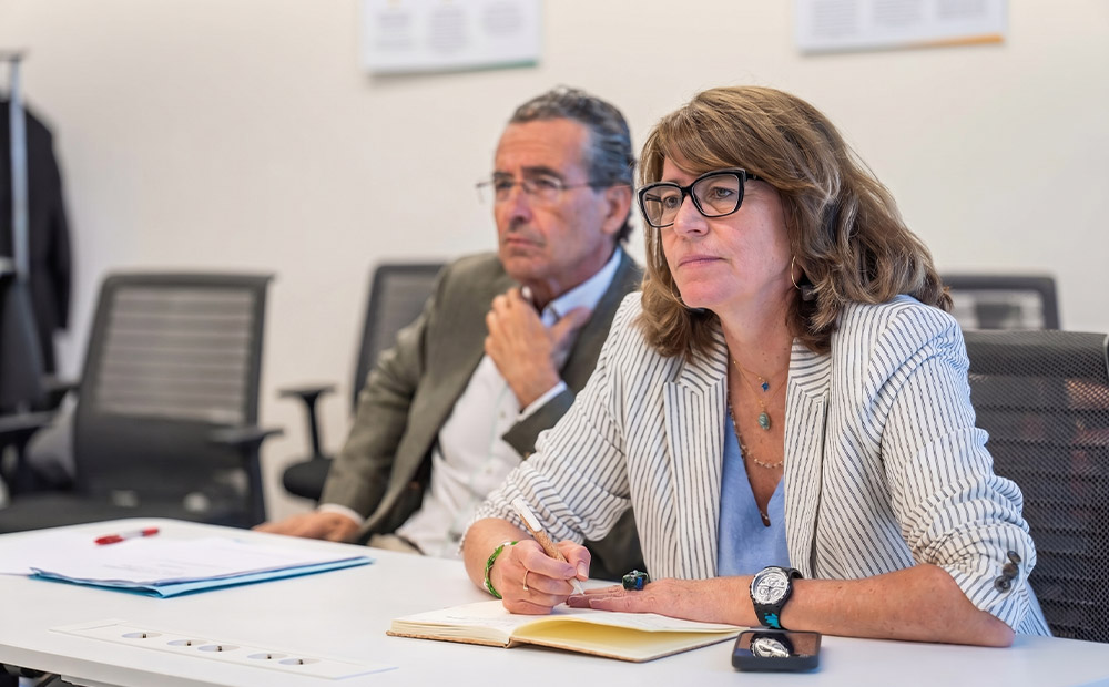 La imagen muestra a profesionales en una reunión de trabajo observando información y tomando notas en un entorno corporativo. La composición transmite la importancia de la reflexión, el análisis y la coordinación entre diferentes áreas para afrontar retos empresariales complejos. 