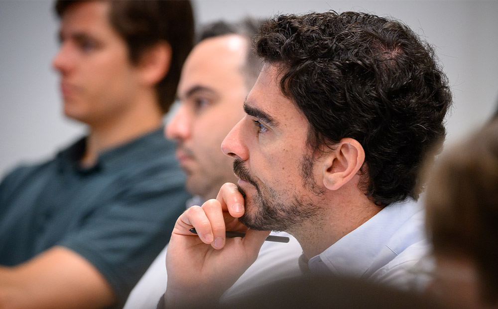 La imagen muestra a varios profesionales siguiendo atentamente una sesión de formación, tomando notas y analizando información en un entorno de aprendizaje ejecutivo