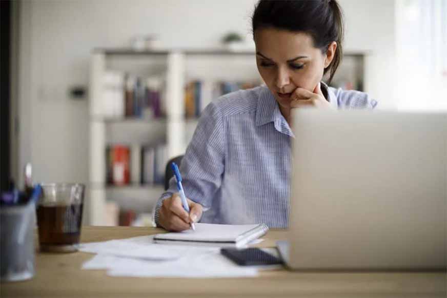 Mujer tomando notas frente a un portátil