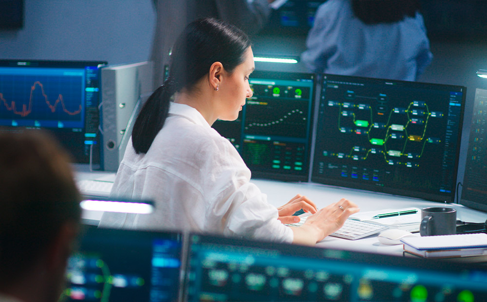 Una ejecutiva analiza datos y genera reportes detallados en una oficina, utilizando múltiples pantallas para visualizar gráficas y analíticas clave.