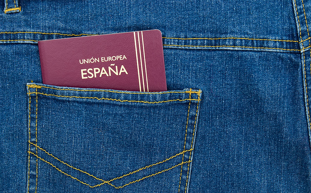 The image shows a maroon-colored Spanish passport peeking out of the back pocket of a pair of jeans. This visual element symbolizes international mobility and legal access to Spanish territory—key aspects for those applying for a Student Visa. Obtaining this visa allows international students to reside in Spain during their academic studies.  