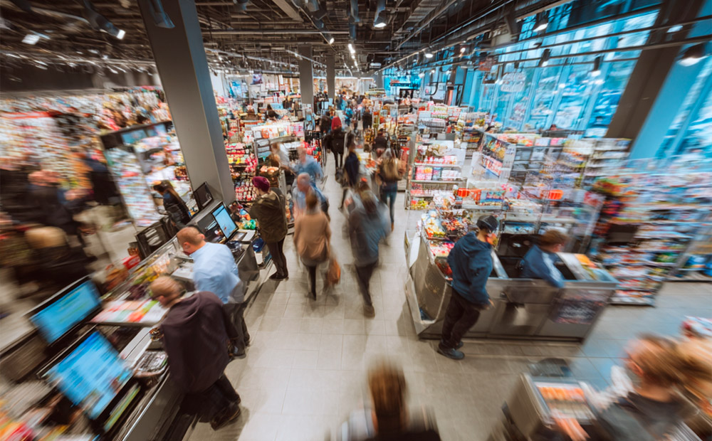A bustling supermarket filled with customers browsing the aisles and checking out at the registers.