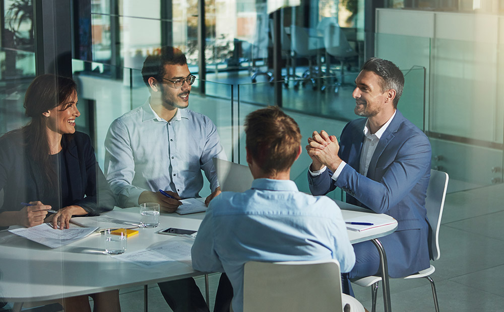Four people are gathered in a modern office, participating in a meeting with documents and notebooks on the table. This scene represents collaborative work among professionals from legal, technical, and business fields—essential for addressing the challenges of environmental law in the energy transition. It illustrates how coordination across sectors enables the development of sustainable policies, compliance with environmental regulations, and progress toward more responsible energy systems.  