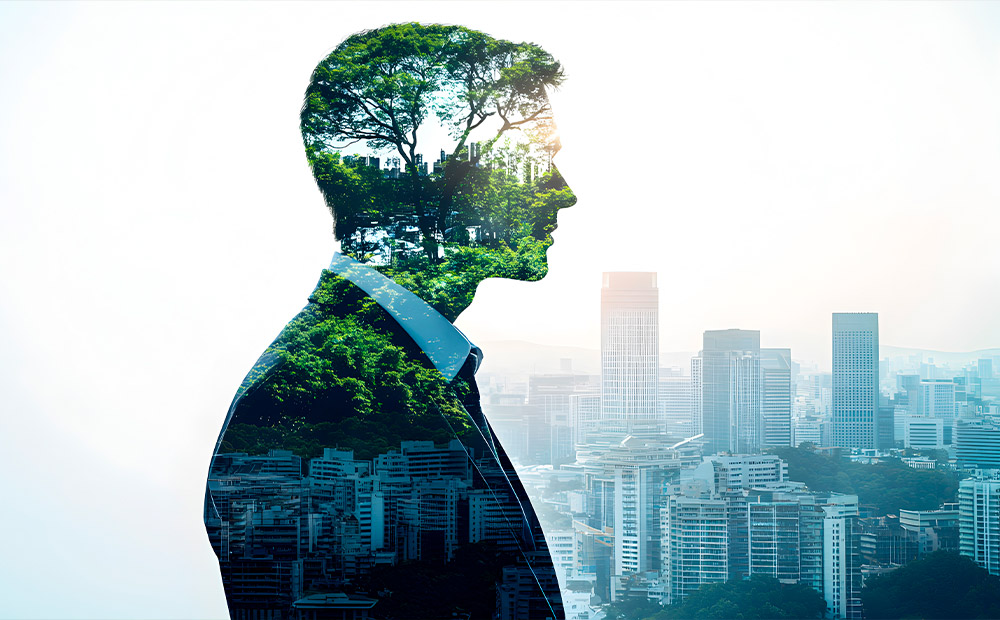 The image shows the silhouette of a person blended with a lush green landscape full of trees, merged with the view of a modern city in the background.