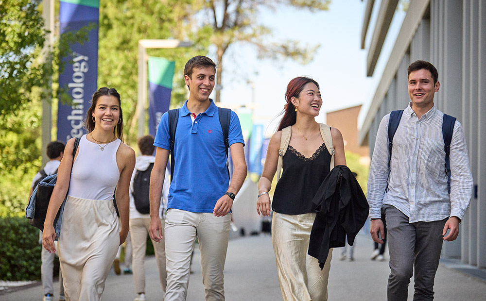 The image shows several individuals walking across the Esade campus with backpacks and study materials, reflecting an academic and learning environment.